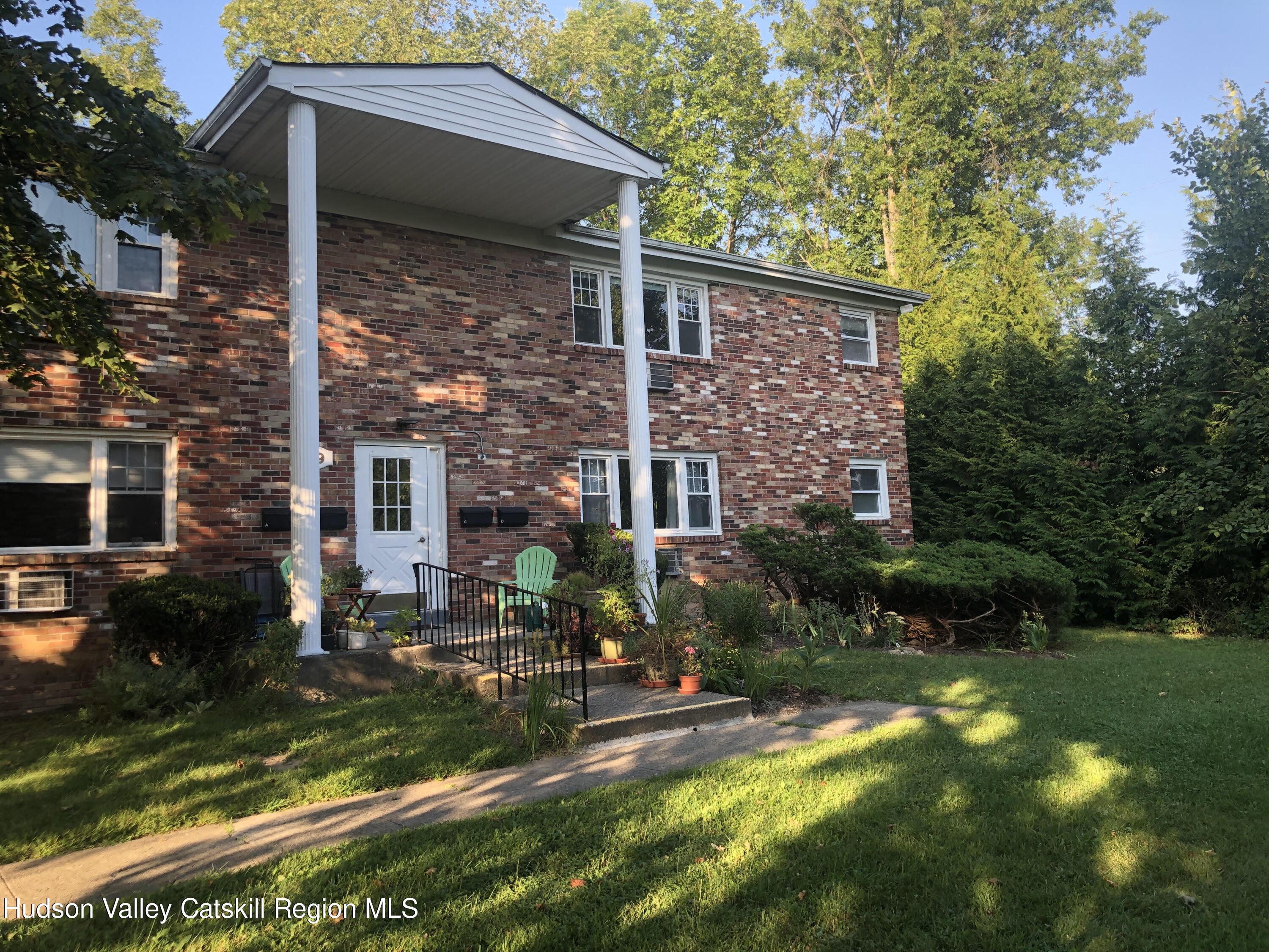 a view of a brick house with a yard plants and large tree