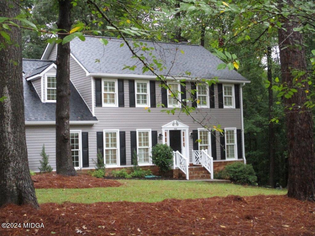 a view of a brick house with a yard plants and large tree