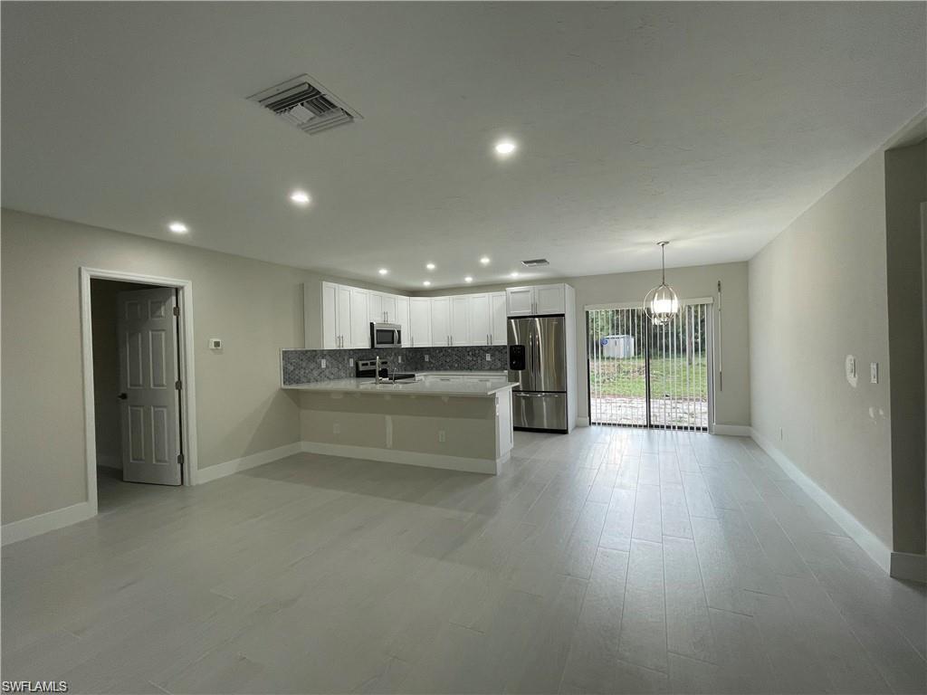 Kitchen with white cabinetry, hanging light fixtures, backsplash, kitchen peninsula, and appliances with stainless steel finishes