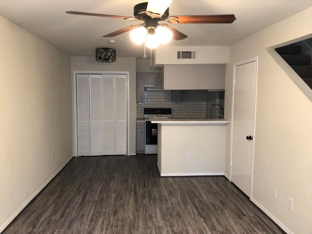 an empty room with wooden floor a ceiling fan a kitchen and a sink