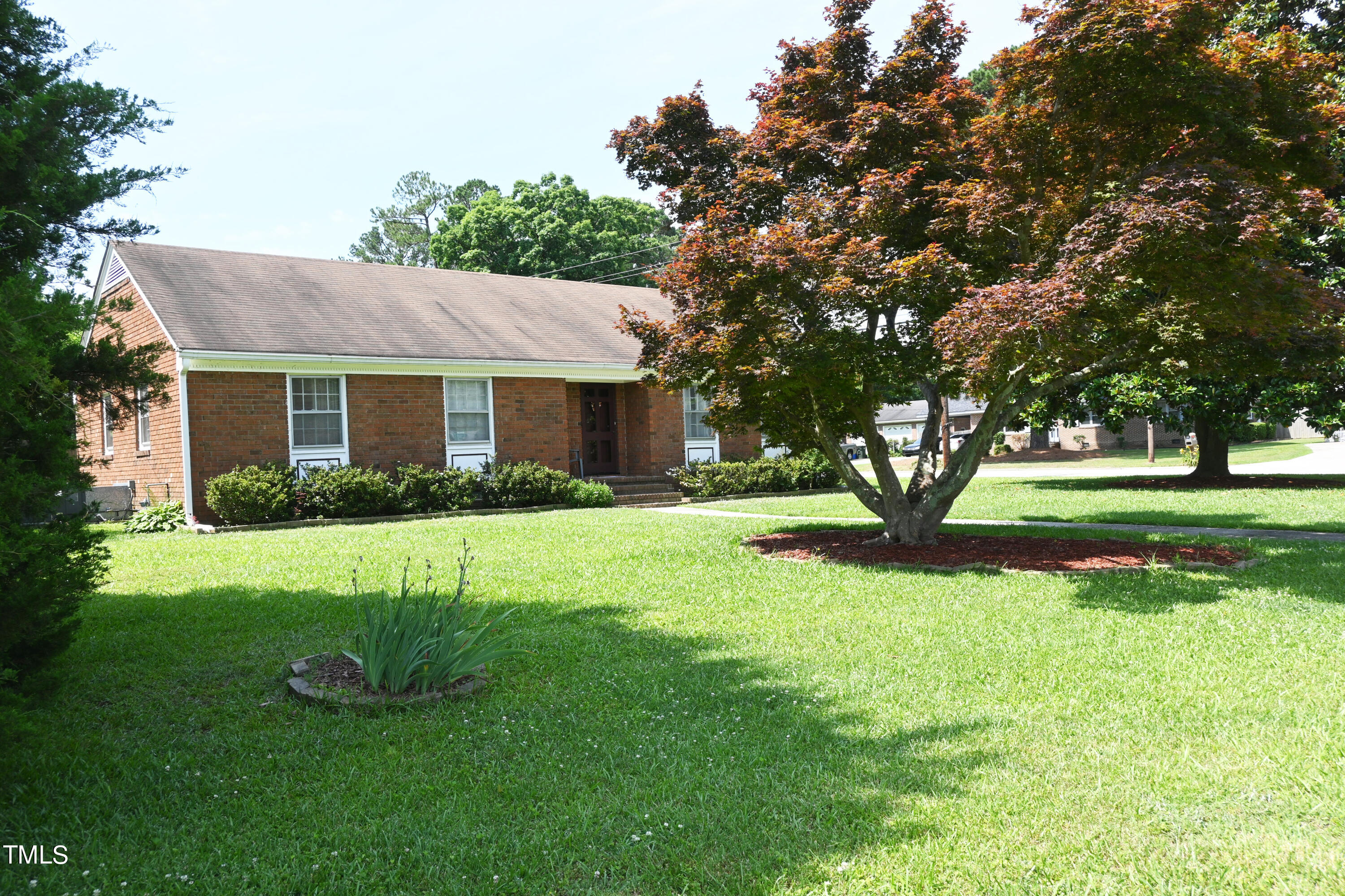 a view of house in front of a big yard with large trees