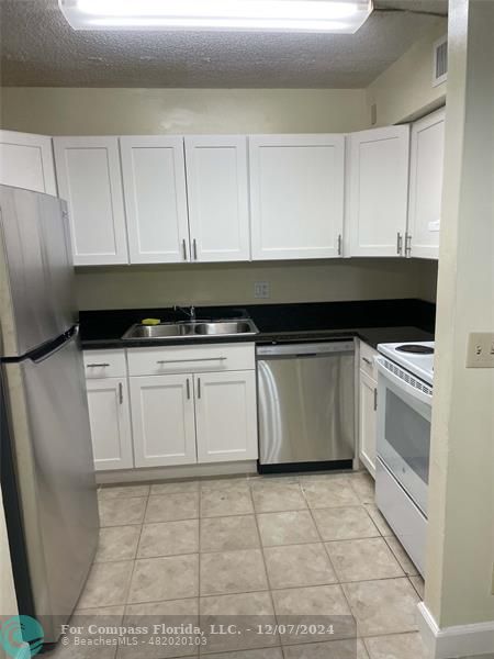 a white kitchen with granite countertop a stove a sink and white cabinets