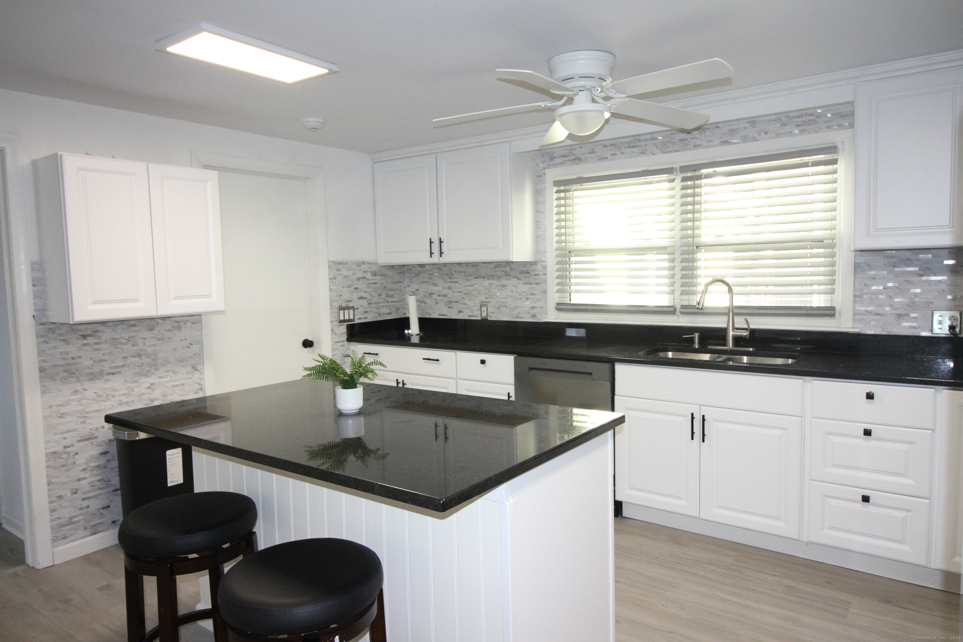 a kitchen with granite countertop a sink a stove white cabinetry and dining table with wooden floor