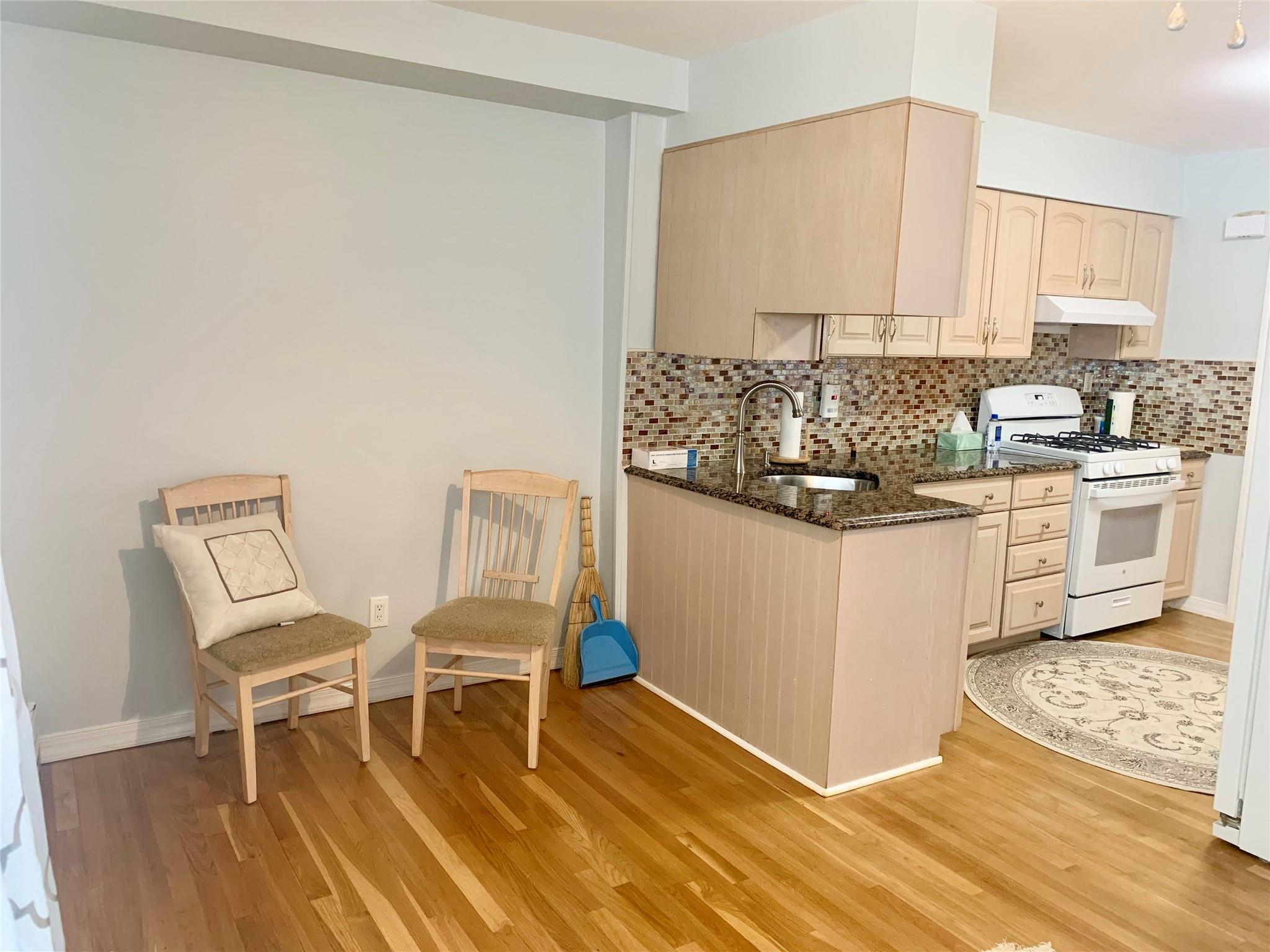 Kitchen with light brown cabinetry, white gas range oven, backsplash, light hardwood / wood-style flooring, and dark stone countertops