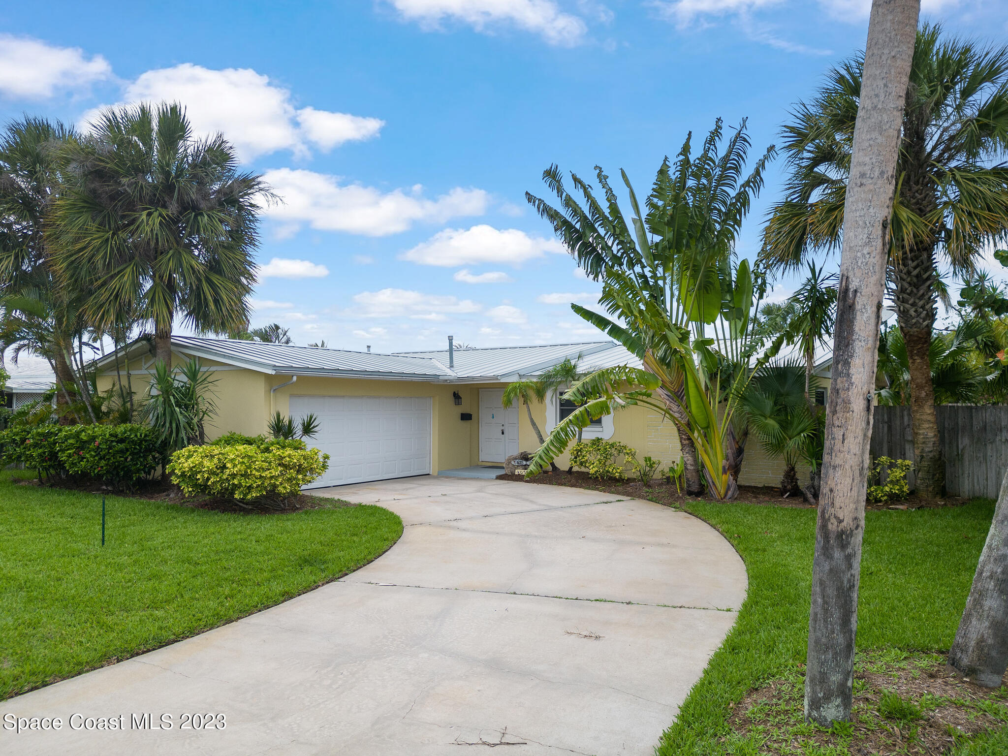 a front view of a house with a garden and palm trees