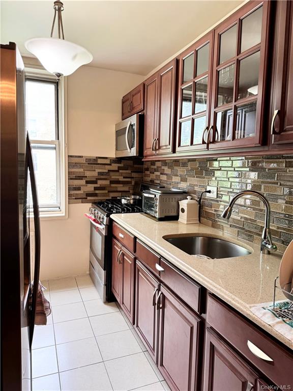 Kitchen with light tile patterned floors, tasteful backsplash, hanging light fixtures, stainless steel appliances, and sink