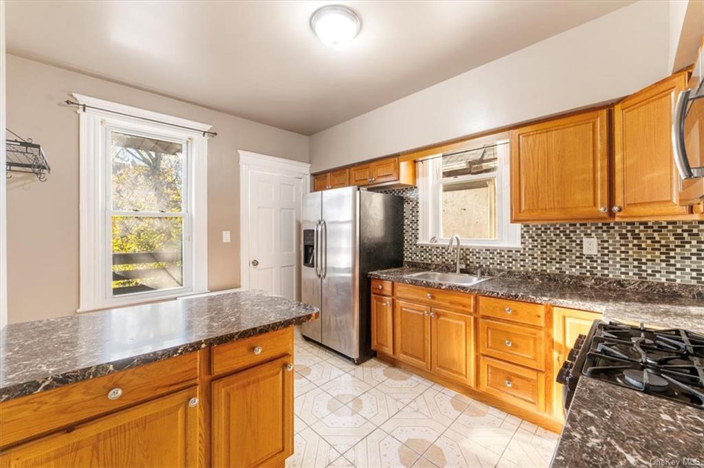 Eat-in-kitchen with sink, backsplash, dark stone counters,   stainless steel appliances, full fridge with ice dispenser. Floor is ceramic tiling