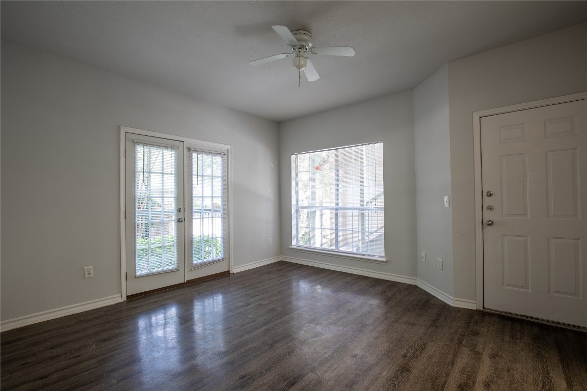 an empty room with wooden floor chandelier fan and windows