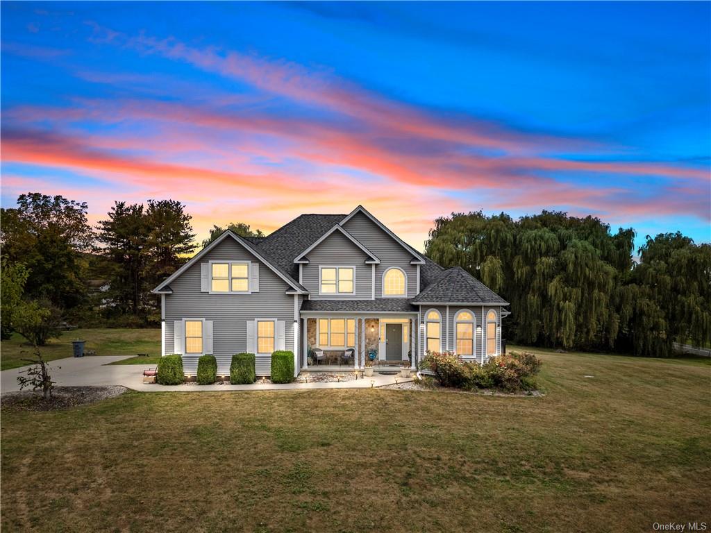 Back house at dusk featuring covered porch and a yard