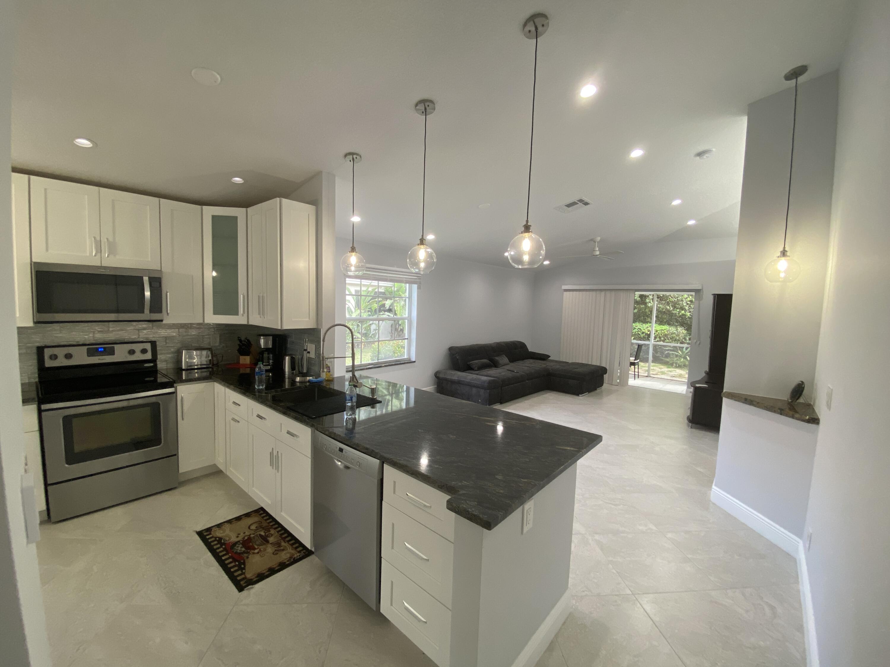 a large white kitchen with a large counter top space a sink stainless steel appliances and cabinets