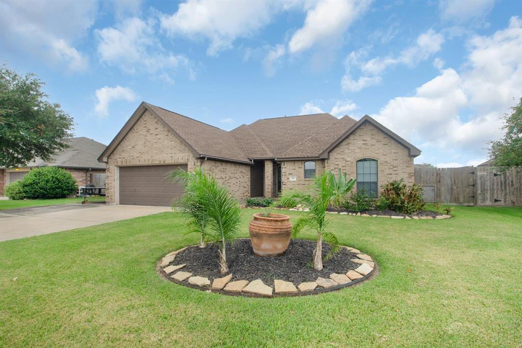 This is a single-story brick home featuring a well-kept lawn, a two-car garage, and a landscaped garden with a decorative pot centerpiece.