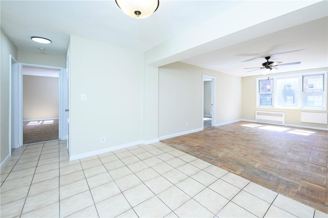 Empty room featuring light parquet floors, radiator, and ceiling fan