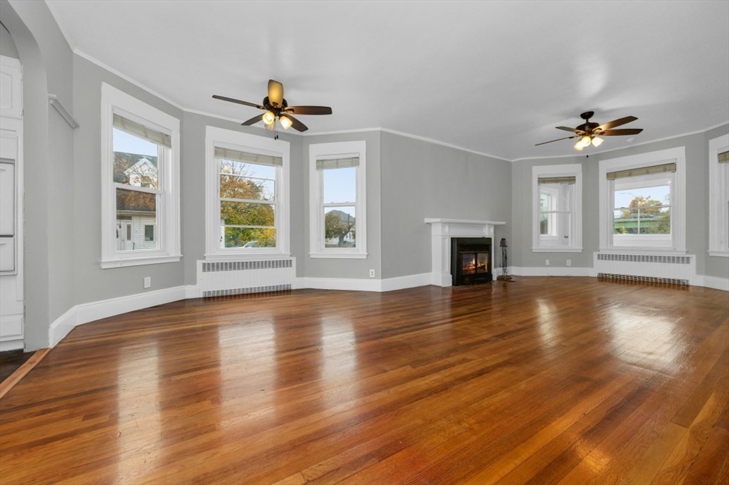 an empty room with wooden floor chandelier fan and windows