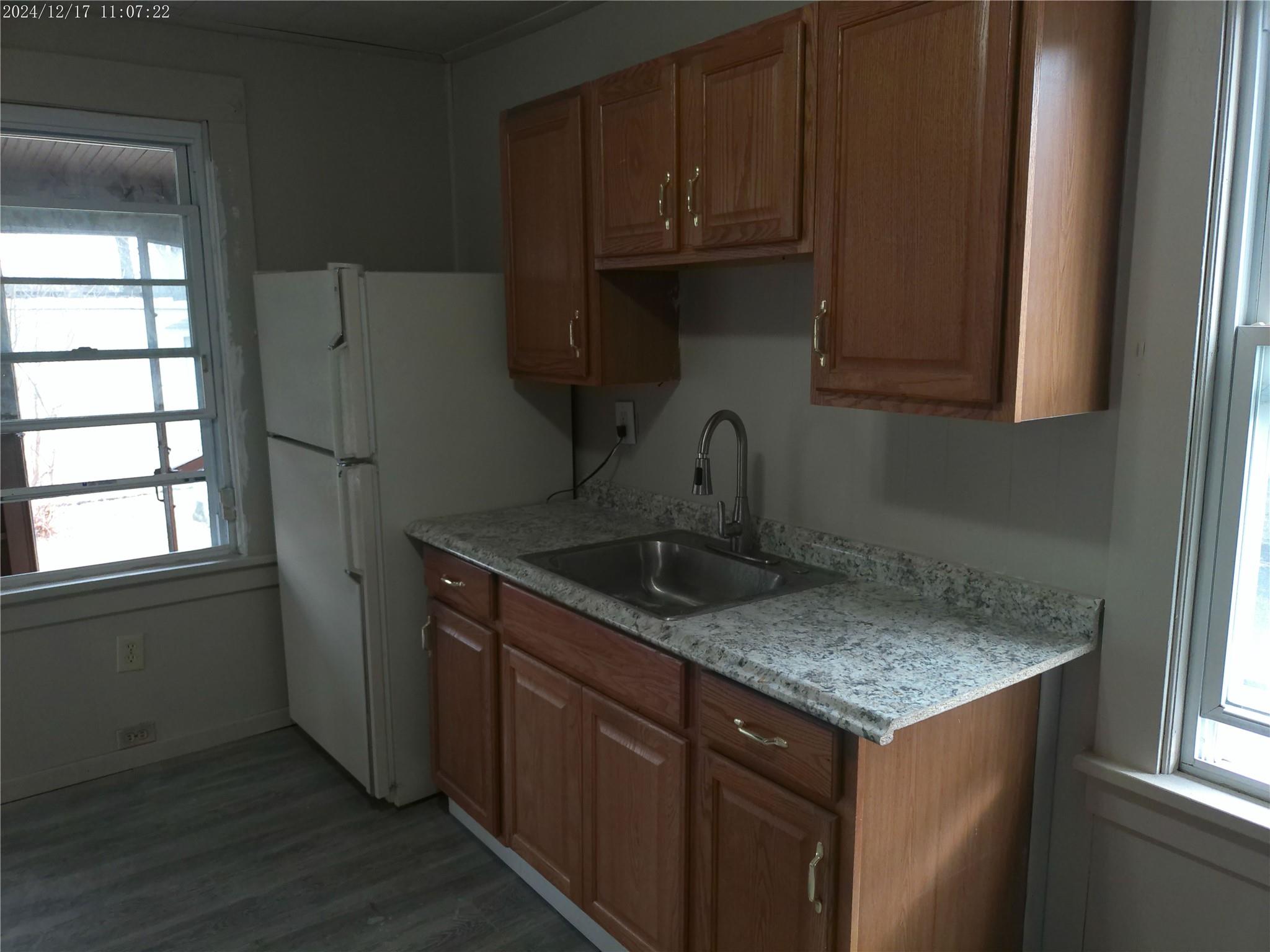 Kitchen featuring dark hardwood / wood-style flooring, white refrigerator, light stone counters, and sink