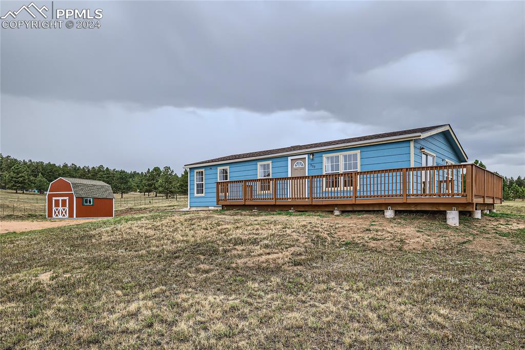 View of front of property featuring a storage unit, a wooden deck, and a front lawn