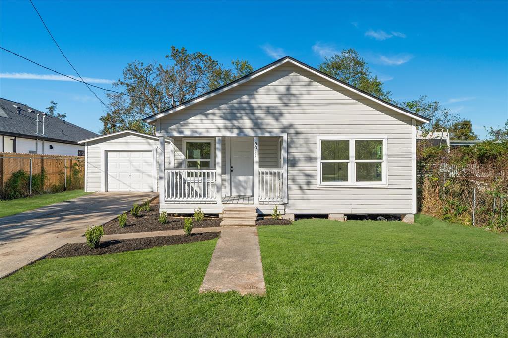 Single-story home with updated siding, a small porch, and a detached garage, framed by a paved driveway and manicured lawn.