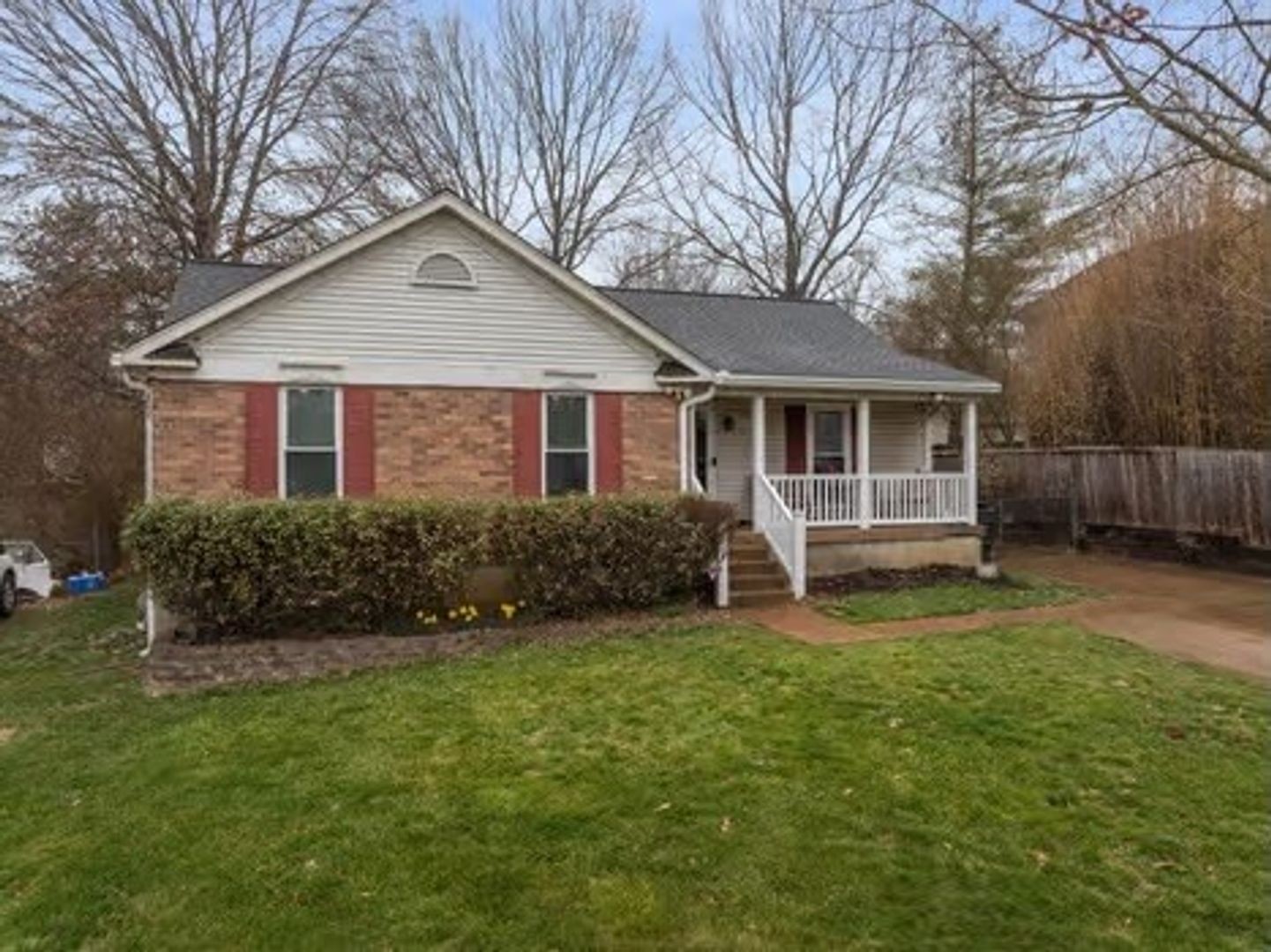 a white house that has a small yard and large trees with wooden fence