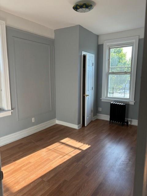 Empty room featuring dark hardwood / wood-style floors and radiator