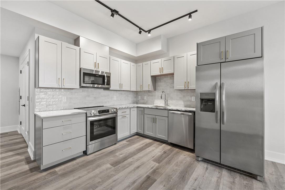 Kitchen with gray cabinets, light wood-type flooring, sink, stainless steel appliances, and backsplash