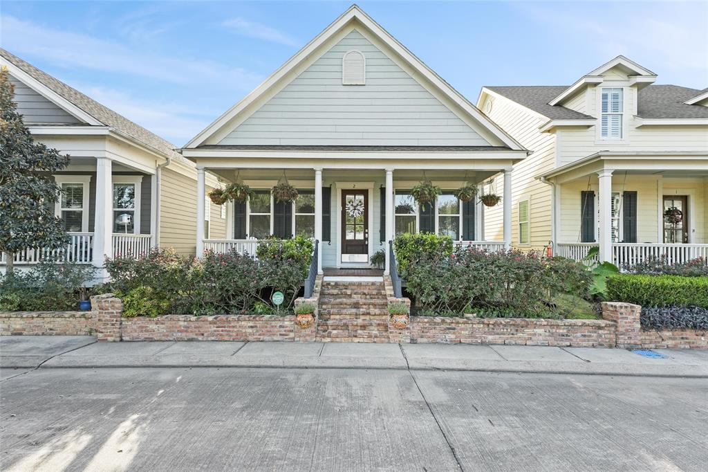 This charming home in the desirable Evia community near Galveston's West End features classic Southern-style architecture, a welcoming brick staircase, a spacious front porch with hanging planters, and lush landscaping that adds to its curb appeal.