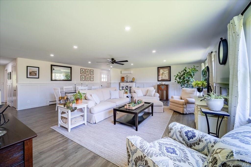 Living room with a wall mounted air conditioner, ceiling fan, light hardwood / wood-style floors, and a baseboard heating unit