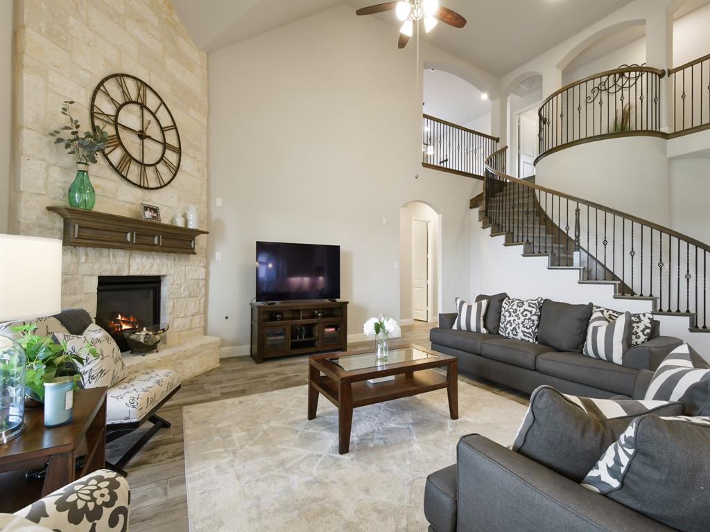 Living room with light hardwood / wood-style floors, a stone fireplace, ceiling fan, and high vaulted ceiling