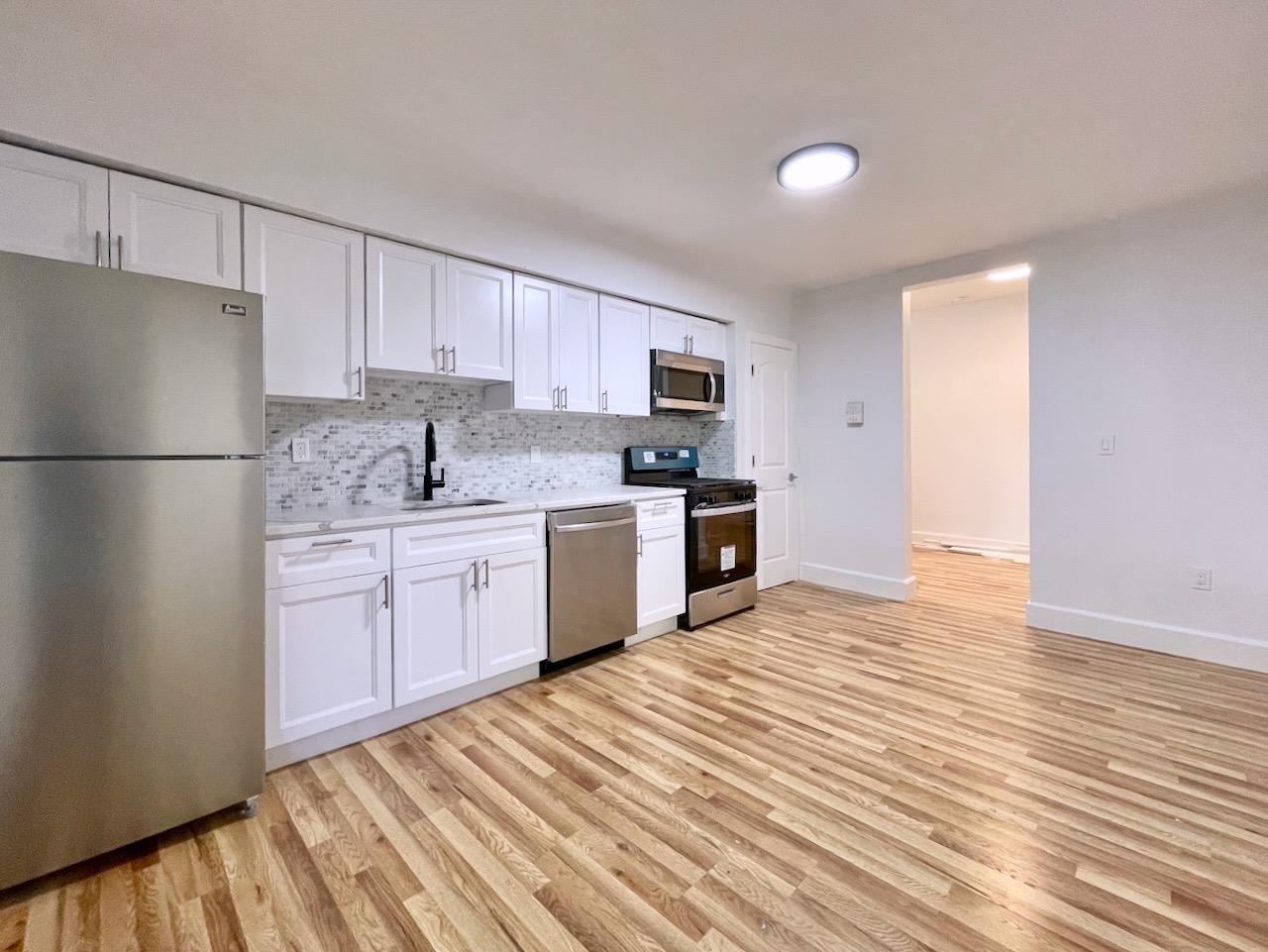 a kitchen with a sink dishwasher a refrigerator with white cabinets and wooden floor