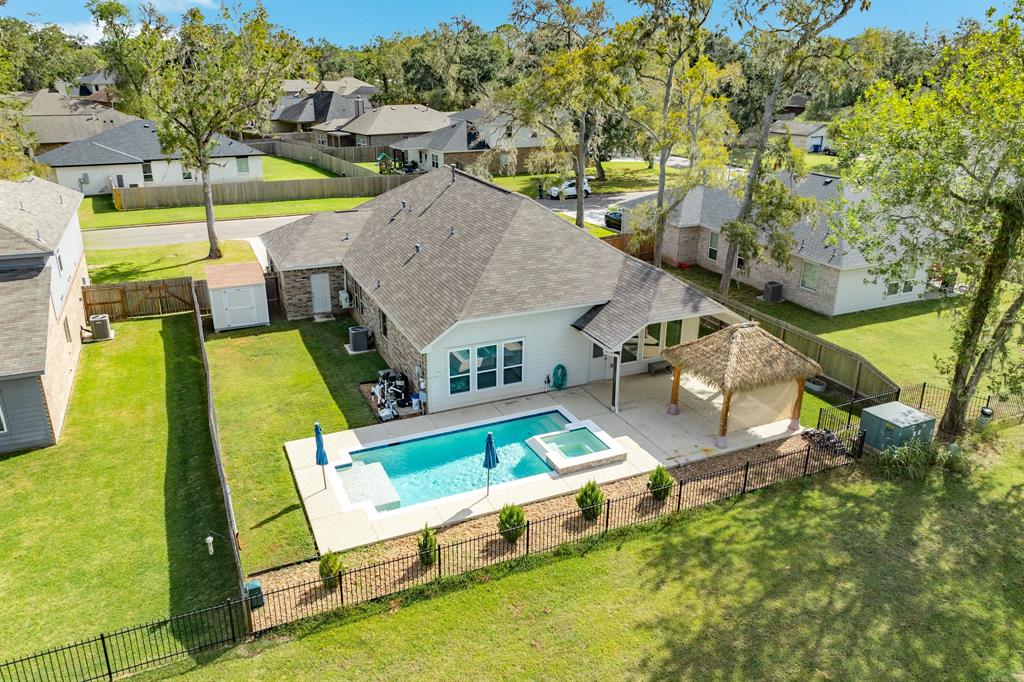 This is a single-family home featuring a spacious backyard with an in-ground pool, a hot tub, and a covered patio area with a thatched-roof structure, all enclosed by a metal fence. 