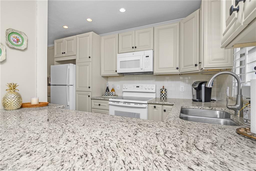 Kitchen featuring tasteful backsplash, light stone counters, sink, and white appliances.