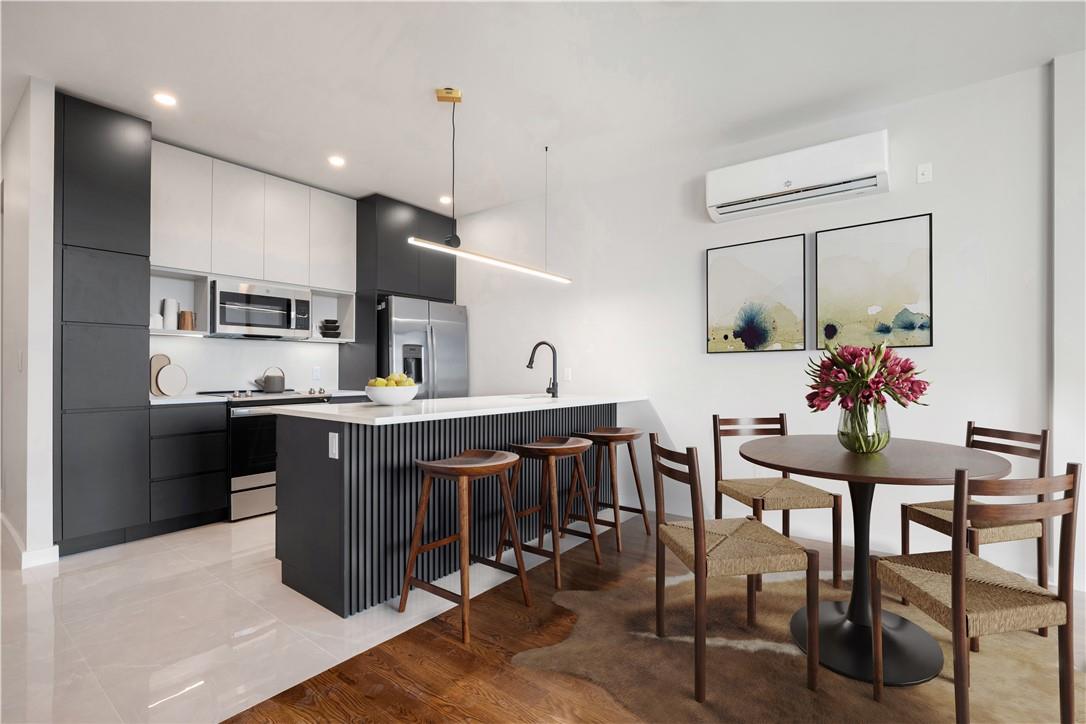 Kitchen with white cabinetry, stainless steel appliances, light hardwood / wood-style flooring, decorative light fixtures, and a wall mounted air conditioner