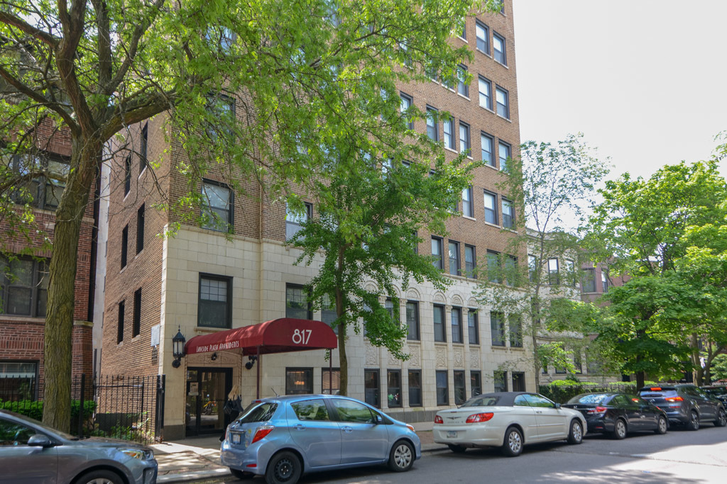 a front view of a building with lot of cars and trees