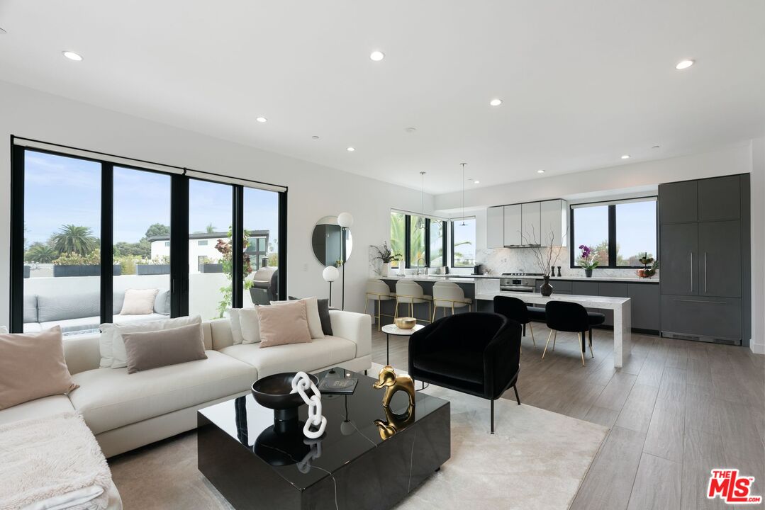 a living room with furniture potted plant kitchen view and a large window