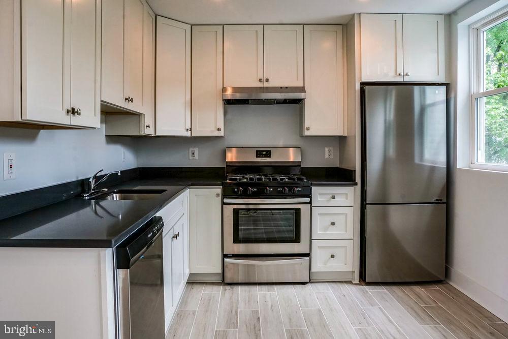 a kitchen with granite countertop a refrigerator stove and white cabinets