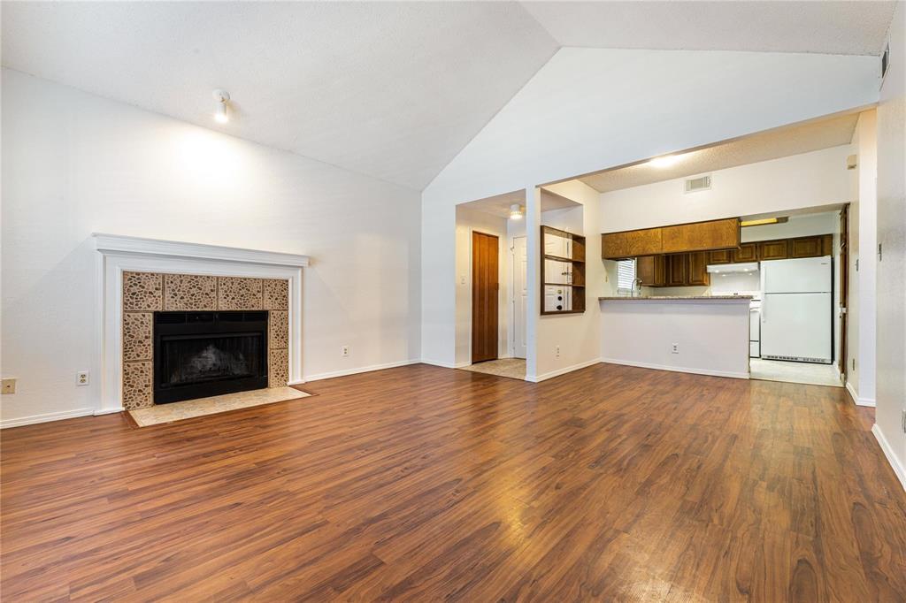 a view of an empty room with wooden floor fireplace and a window