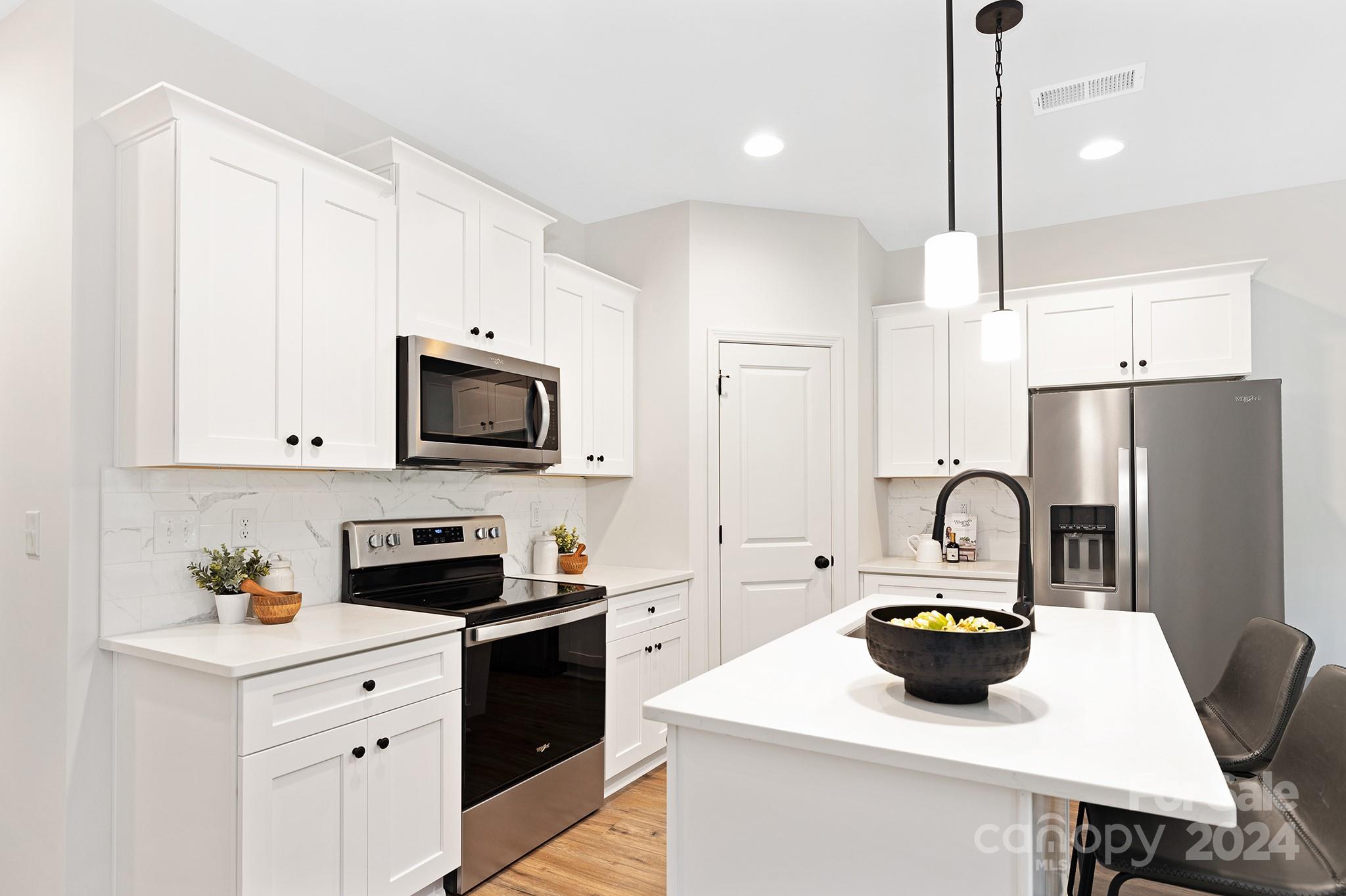 a kitchen with a refrigerator a stove a sink and white cabinets with wooden floors