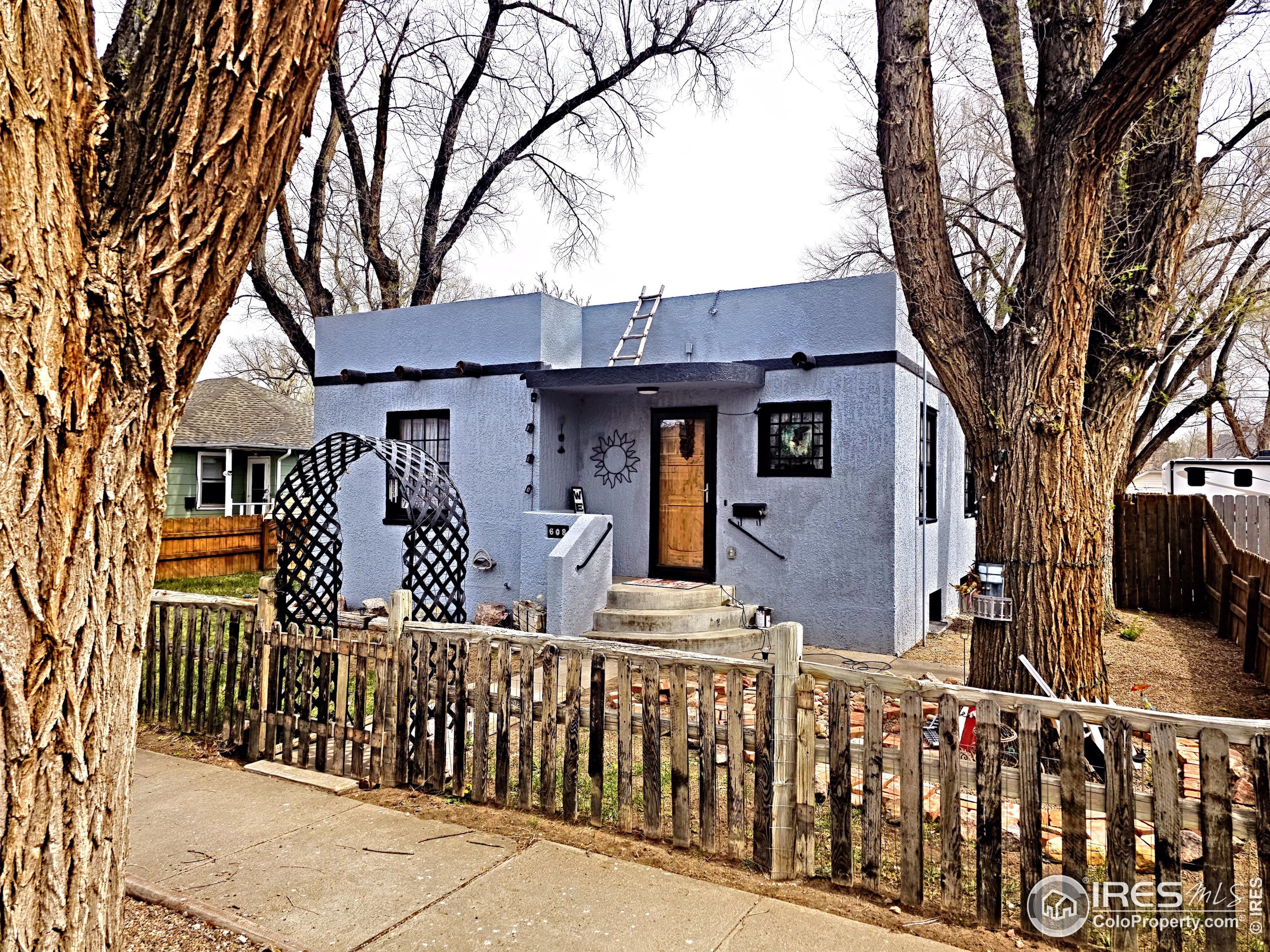 a front view of house with large trees and wooden fence