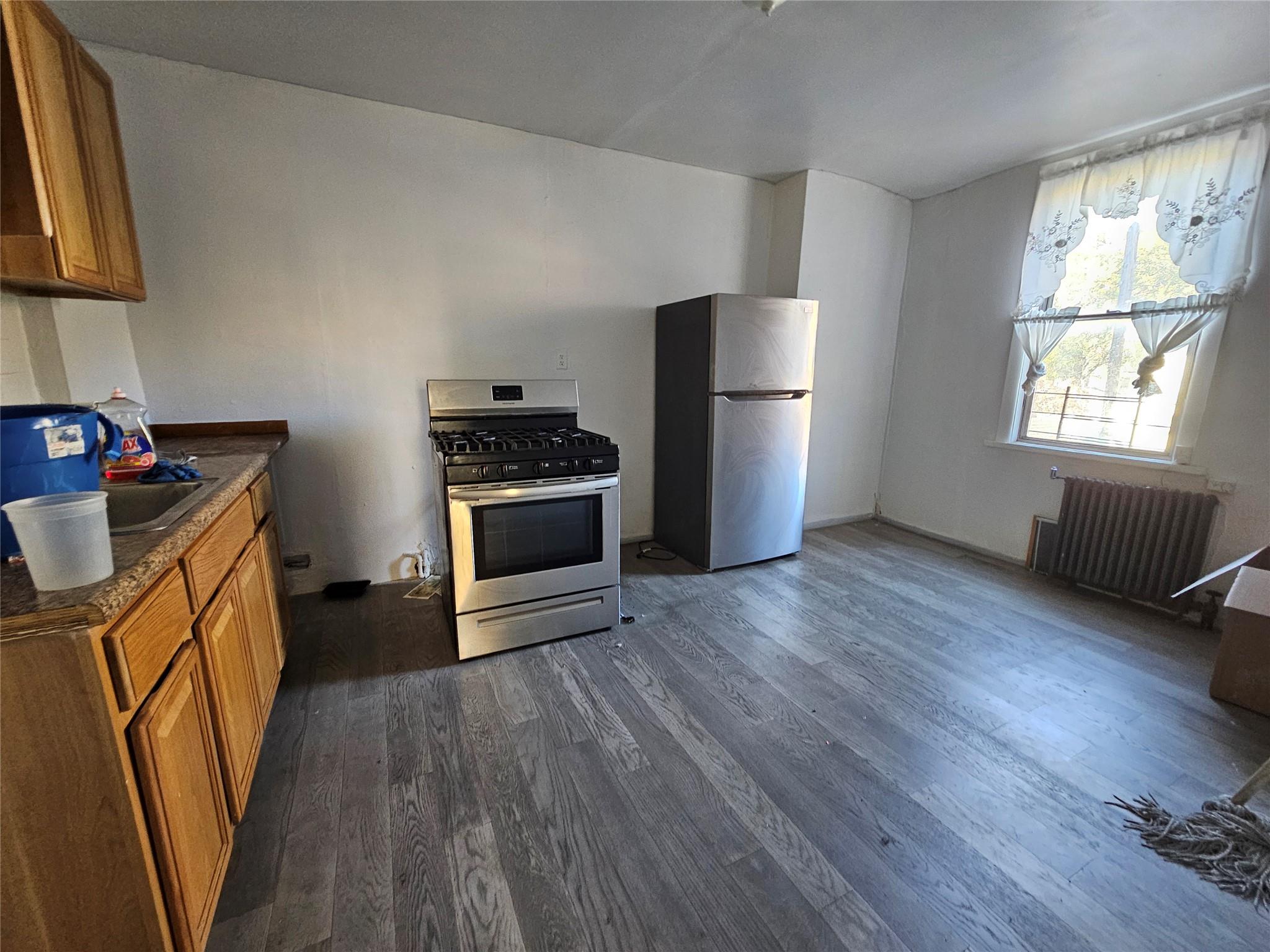 Kitchen featuring dark hardwood / wood-style flooring, radiator heating unit, sink, and appliances with stainless steel finishes