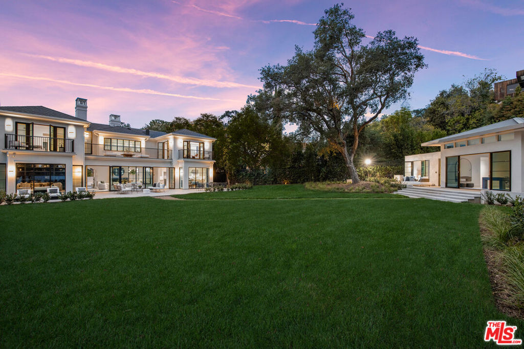 a view of house in front of a big yard with large trees