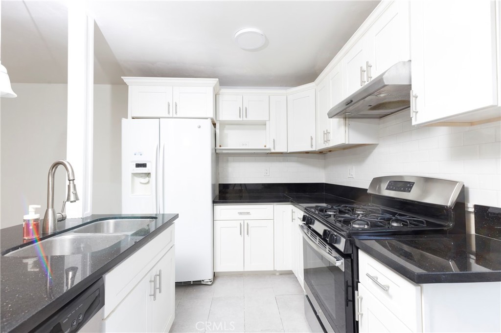 a kitchen with granite countertop a sink stainless steel appliances and white cabinets