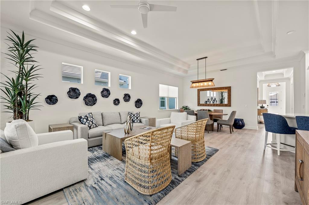 Living room with ceiling fan, a raised ceiling, and light wood-type flooring