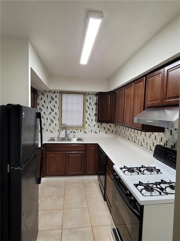 Kitchen with wall chimney exhaust hood, sink, dark brown cabinets, light tile floors, and black appliances