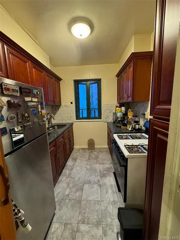 Kitchen featuring stainless steel fridge, backsplash, white gas range oven, sink, and dark stone counters