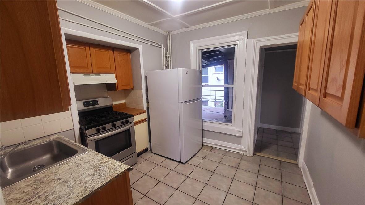 Kitchen featuring white refrigerator, sink, stainless steel gas range oven, backsplash, and light stone countertops