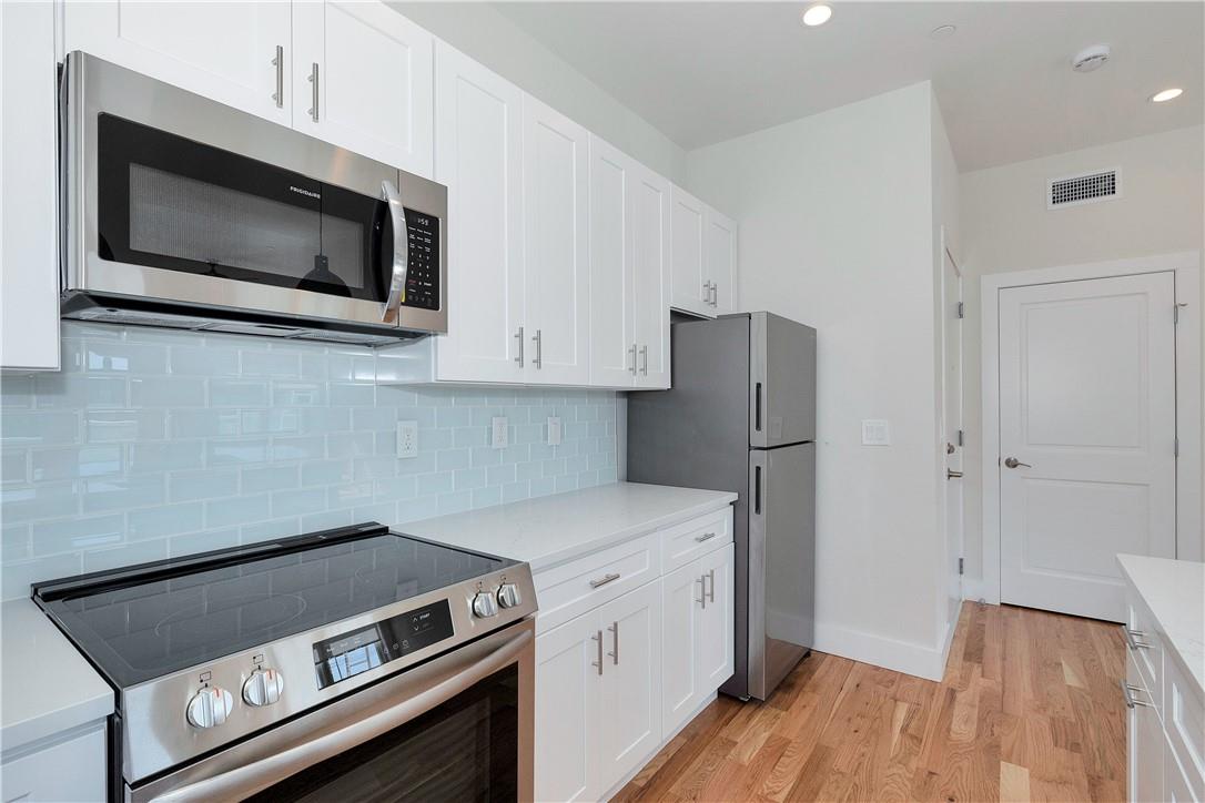 Kitchen featuring stainless steel appliances, light wood-type flooring, white cabinetry, and tasteful backsplash