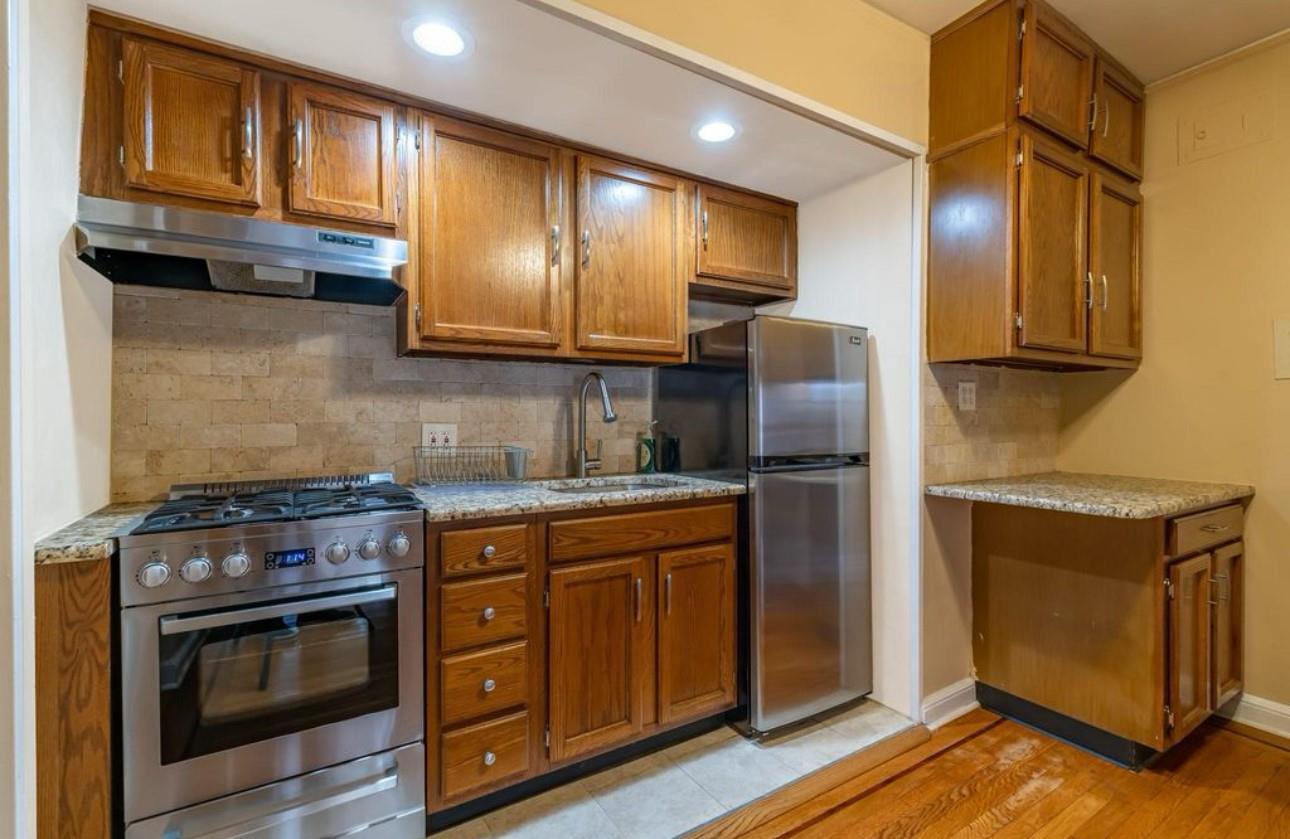 Kitchen featuring sink, light wood-type flooring, tasteful backsplash, light stone counters, and stainless steel appliances