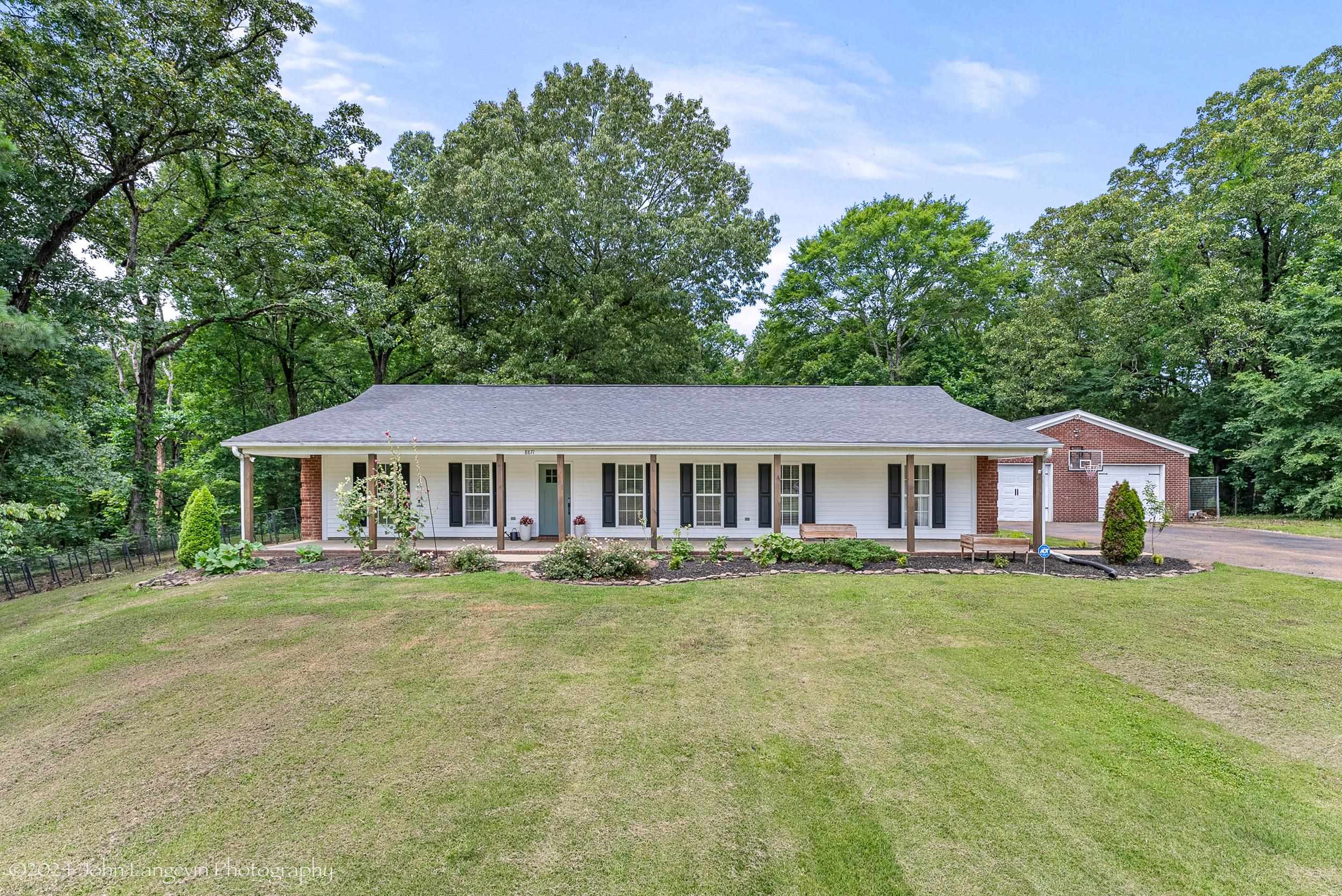 Ranch-style home featuring a garage, a front lawn, and covered porch