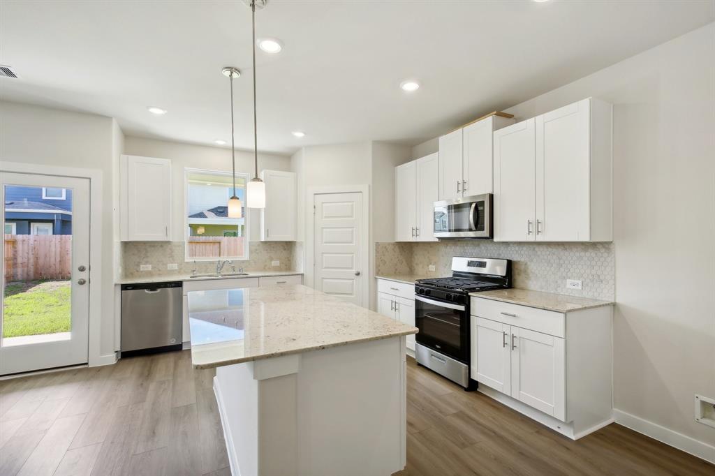 a large kitchen with granite countertop a stove a sink a center island and stainless steel appliances