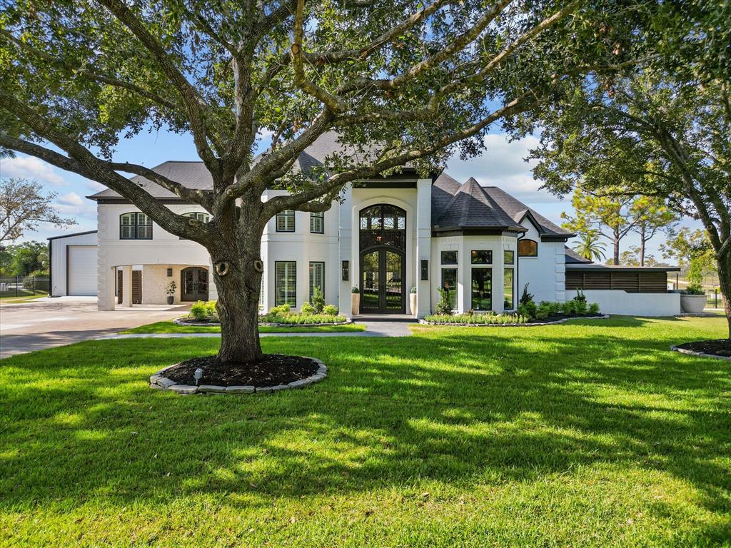 This is a spacious, two-story home featuring a large front yard with mature trees, a grand entrance with tall windows, and a mix of modern and traditional architectural elements.