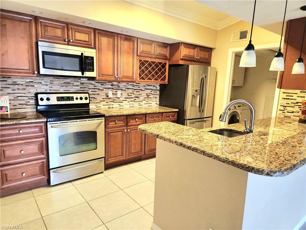 Kitchen featuring kitchen peninsula, appliances with stainless steel finishes, light stone counters, sink, and pendant lighting