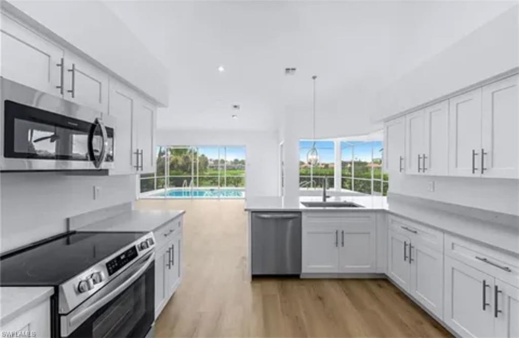 Kitchen with white cabinets, appliances with stainless steel finishes, light wood-type flooring, pendant lighting, and sink